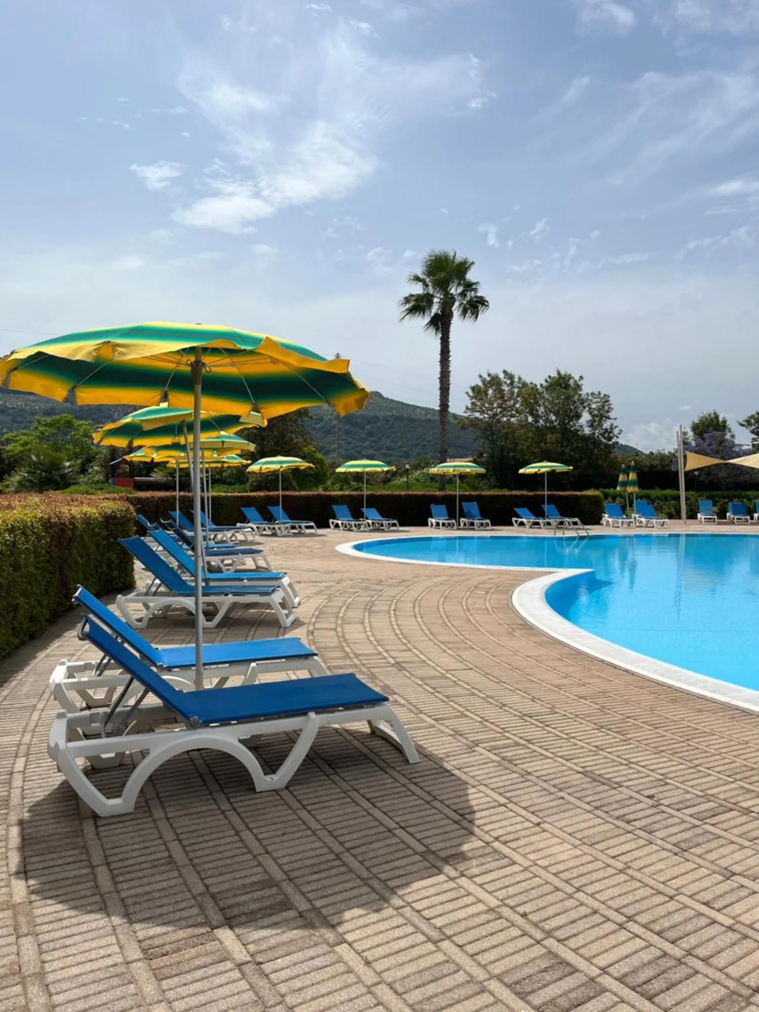 Piscina del Pizzo Beach Club con lettini blu e ombrelloni a righe verdi e gialle