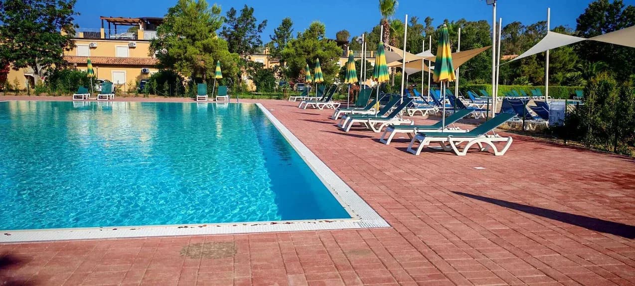 Piscina tra le palazzine del complesso, con lettini e vele ombreggianti