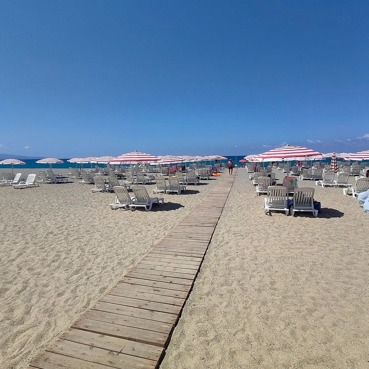 Spiaggia privata del Pizzo Beach Club con passerella in legno, lettini e ombrelloni a righe bianche e rosse